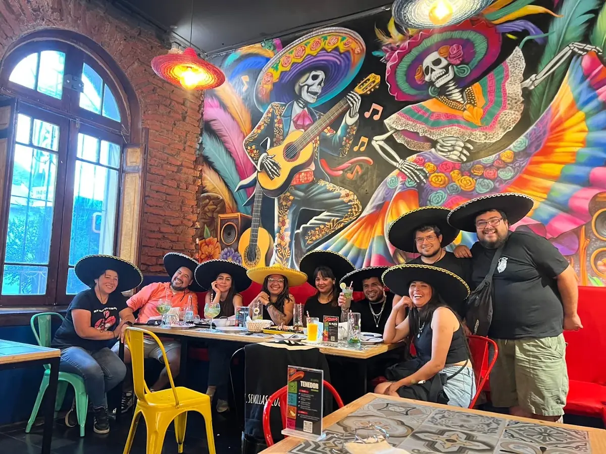 Mesa de amigos con sombreros frente al mural de catrinas mariachi